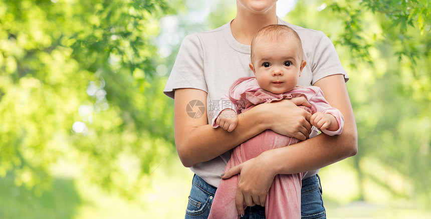 家庭,孩子父母的快乐的微笑轻母亲抱着小女儿绿色的自然背景快乐的轻母亲抱着小女儿图片