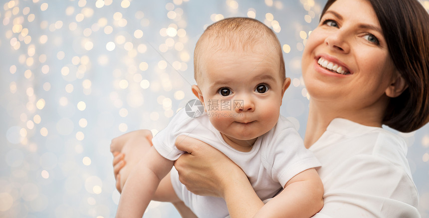 家庭,孩子父母的快乐的微笑中母亲抱着小宝贝女儿节日的灯光背景快乐的中母亲小女儿图片