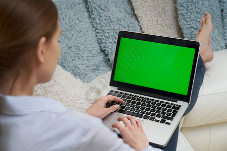 肩膀上看女人躺沙发上用绿色屏幕笔记本电脑图片