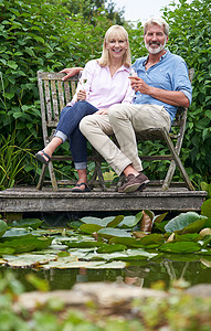 成熟夫妇的肖像庆祝与香槟坐椅子上木制码头湖边图片