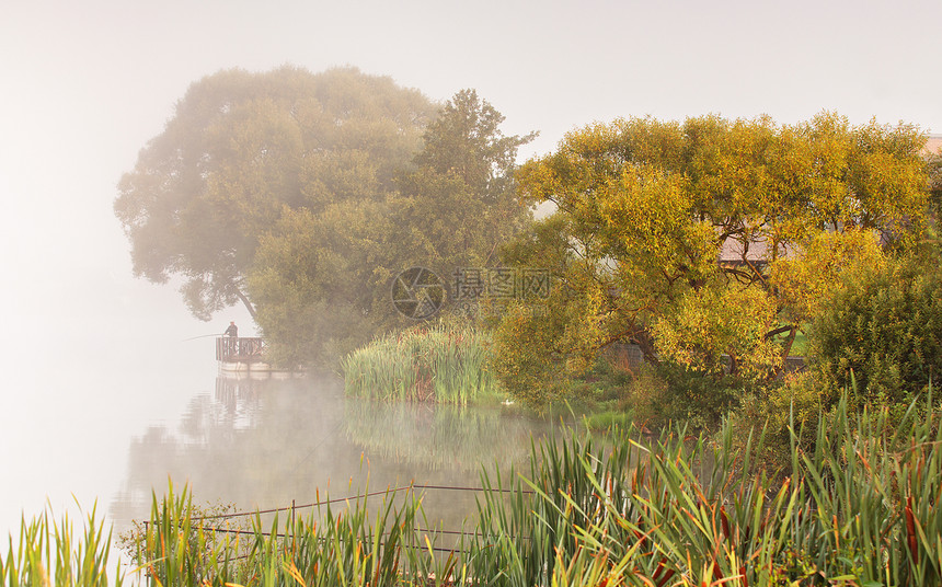 雾湖上钓鱼渔夫带着杆子湖上,宁静的水,倒影深雾寒冷的秋天早晨,白俄罗斯图片