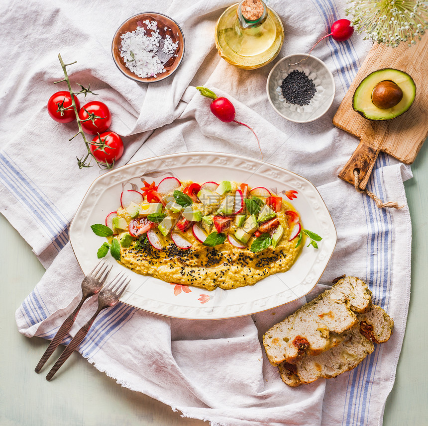 美味的鹰嘴豆泥盘子,橄榄油鳄梨新鲜蔬菜草药,放厨房的桌子上,叉子包,风景素食食品的健康图片