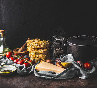 塔利亚泰尔黑暗的乡村厨房柜台上自制的意大利,锅新鲜的食材,用于美味的烹饪西红柿橄榄油帕尔马干酪大蒜洋葱背景