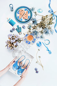 女人的手着白色桌上盒子里的新蓝鞋女的静物与化妆品,花,茶与蛋糕片,珠宝的风景平躺时尚博客背景图片