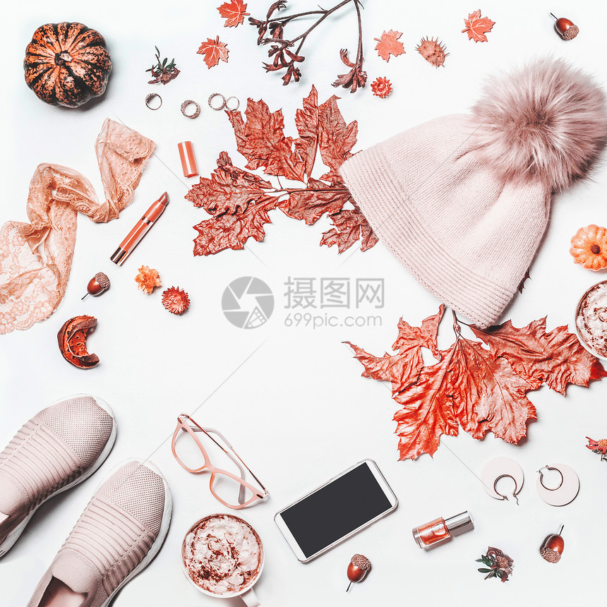 秋季美丽的女安排白色背景与针帽子与POM,南瓜运动鞋,智能手机与模拟,落叶,化妆品杯子与热巧克力的风景平图片