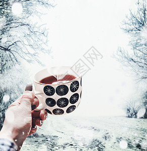 女手着杯带蒸汽的茶,降雪的自然景观中波尔卡点杯与雪花杯茶图片