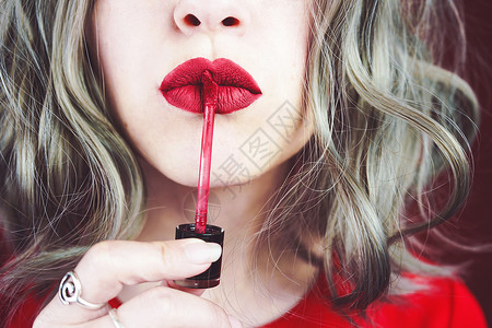 时髦红色咬嘴唇轻的女人用红色的哑光口红给她的嘴唇化妆背景