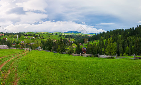 风景如画的春山景象与木制的劈轨围栏穿过片绿色郁郁葱葱的牧场,条乡村公路山谷上的老房子被松树林包围亚布隆尼亚,乌克兰背景图片