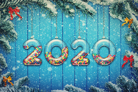 雪花边新快乐2020假期背景透明的数字,由璃制成,装满了五颜六色的糖果糖果,挂雪白的诞树树枝上背景