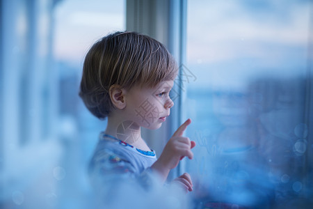 可爱的两岁孩子看着通往城市的窗户柔的蓝色浪漫色调孩子看着窗户图片