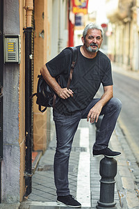 城市背景下成熟的旅游人成熟的男,白发胡须,穿着休闲服装旅行背包背景图片