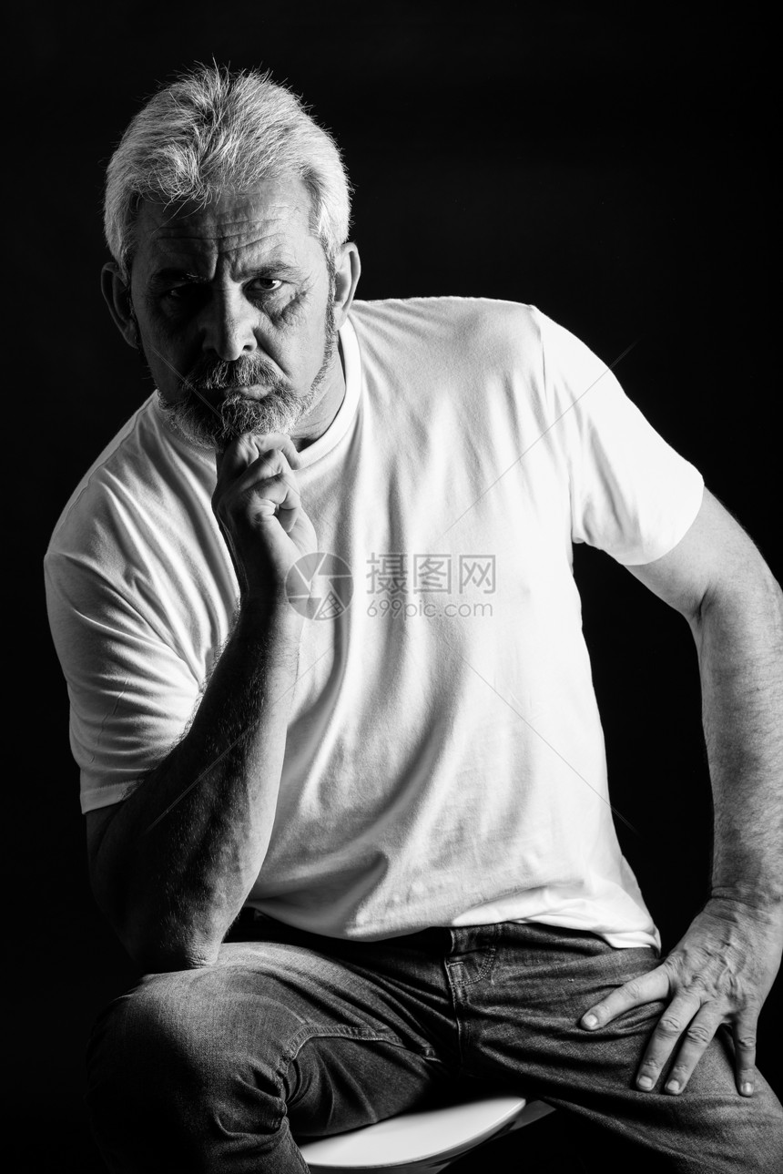 个严肃成熟的男人看着相机的肖像白发胡须的老男,穿着黑色背景上隔离的休闲服装工作室拍摄黑白图片
