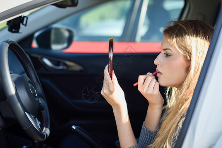 开车女孩金发女人在车里对着镜子涂口红背景