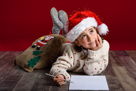 可爱的小女孩戴着诞老人的帽子,木地板上写着诞老人的信诞节的冬天衣服图片
