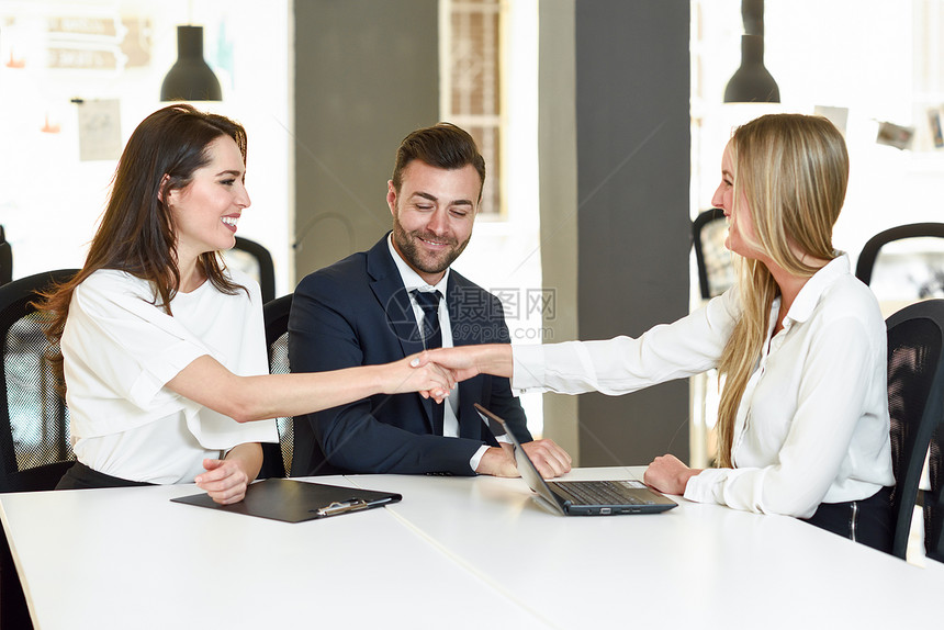 微笑的轻夫妇与保险代理人投资顾问握手三个人办公室开会达成协议图片