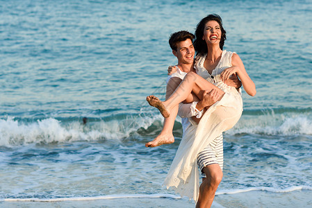 轻的幸福夫妇美丽的海滩上散步趣的男人怀里抱着个女人穿着休闲衣服的人图片
