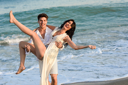 轻的幸福夫妇美丽的海滩上散步趣的男人怀里抱着个女人穿着休闲衣服的人图片