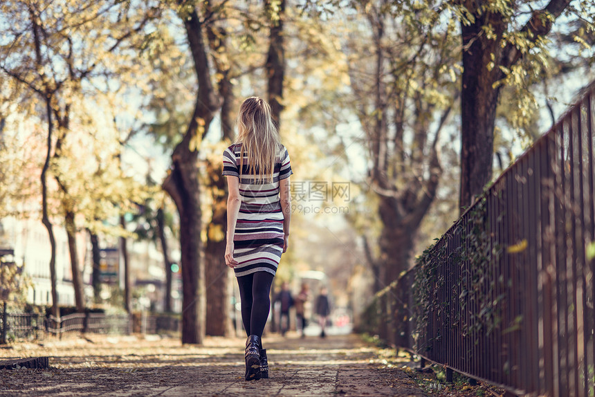 轻的金发女人走街上城市背景的漂亮女孩穿着条纹连衣裙黑色紧身衣直发的女后视图图片