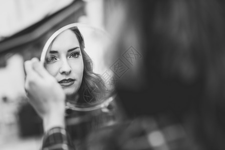 轻女人城市背景中的小镜子里看自己的肖像黑白照片图片