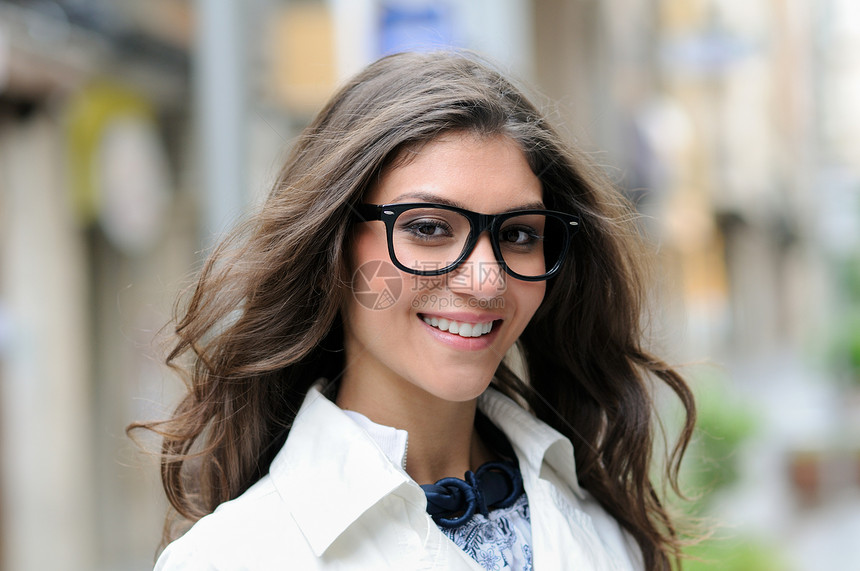 位戴眼镜的漂亮女人的肖像,城市背景下微笑图片