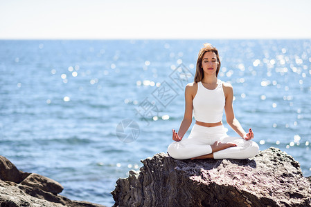 坐在海边石头上练瑜伽的外国女生高清图片