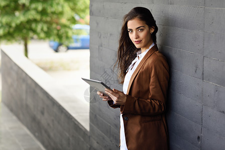 轻的女商人,平板电脑站办公楼外穿正式衣服的漂亮女人穿着棕色夹克的轻女孩图片