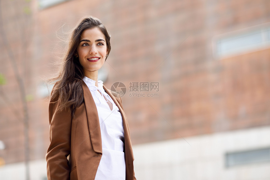 轻的女人,留着漂亮的头发站办公楼外穿正式服装的女商人,留着波浪式发型穿着棕色夹克裤子的轻女孩图片