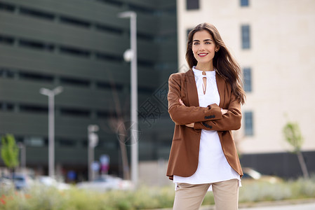 运动夹克轻的女人,留着漂亮的头发站办公楼外穿正式服装的女商人,留着波浪式发型穿着棕色夹克裤子的轻女孩背景