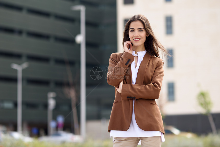 轻的女人,留着漂亮的头发站办公楼外穿正式服装的女商人,留着波浪式发型穿着棕色夹克裤子的轻女孩图片