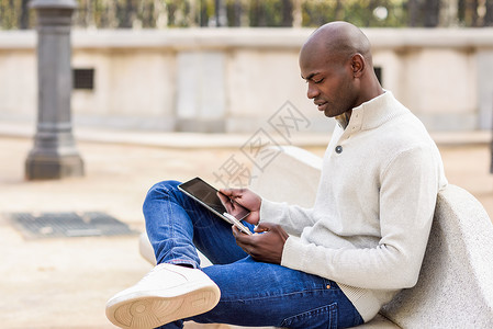 黑人轻人城市背景下看平板电脑智能手机轻的非洲人光头穿着休闲服背景图片