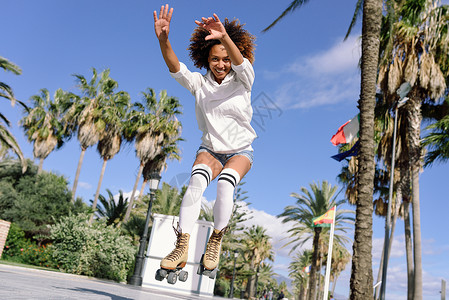 留音机穿着溜冰鞋的轻黑人女人海滩附近跳跃阳光明媚的长廊上留着AFRO发型的女孩背景