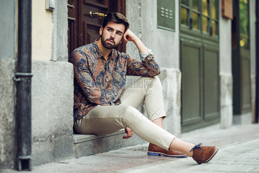 轻的留着胡子的男人,时尚的模特,坐城市的台阶上留着胡子现代发型的家伙街上看着图片