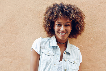 轻的黑人女人,阿夫罗的发型,街上的墙上微笑城市背景下穿休闲衣服的女孩图片