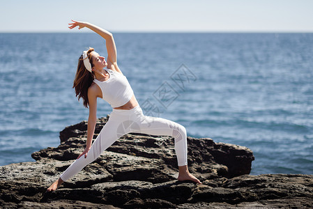 海滩上瑜伽的轻女子女运动员身穿白色运动服,太阳下与海的背景人物图片