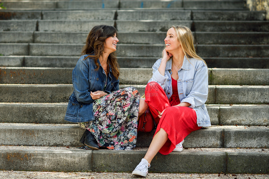 两个轻的女人城市的台阶上谈笑风生两个女孩穿着休闲服生活方式的图片