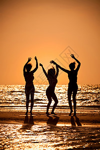 大人全部都要三个穿着比基尼的漂亮轻女人日落时海滩上跳舞,都剪影背景