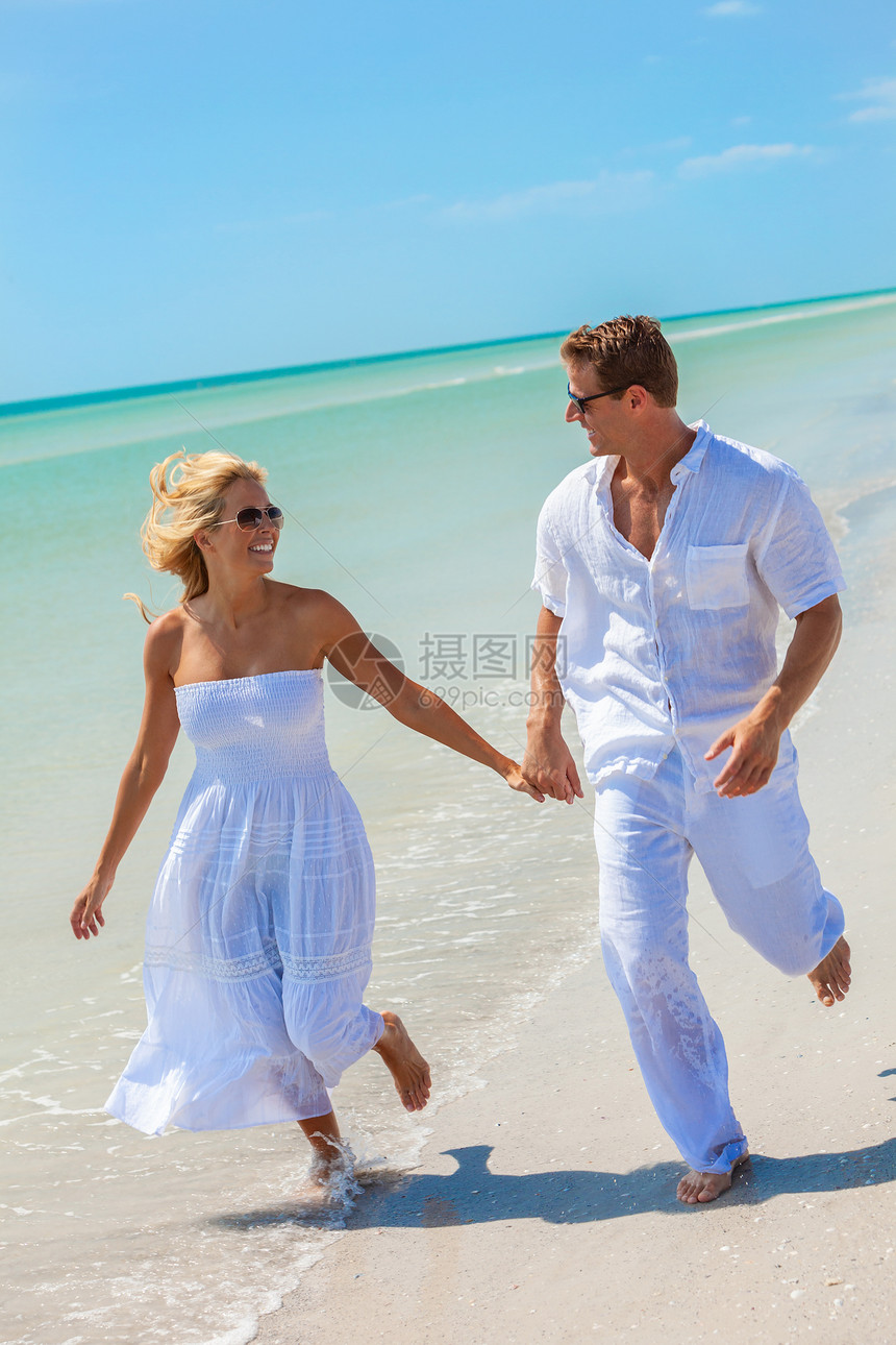 穿着白色衣服的浪漫夫妇牵着手片荒凉的热带海滩上的海水中奔跑,明亮的蓝天图片