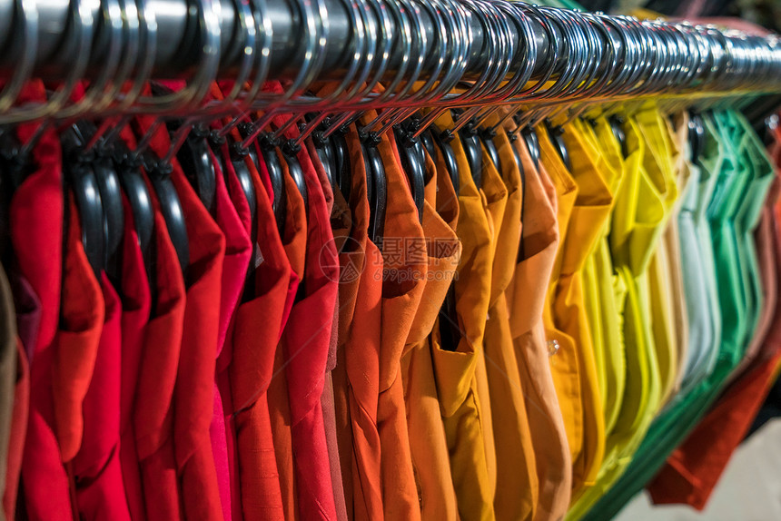 男式衬衫按颜色顺序排列旧货店衣柜壁橱栏杆上的衣架上图片