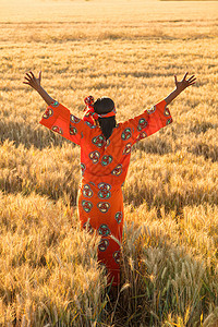 穿着传统衣服的非洲妇女日落日出时站大麦小麦作物的田野上举手臂图片