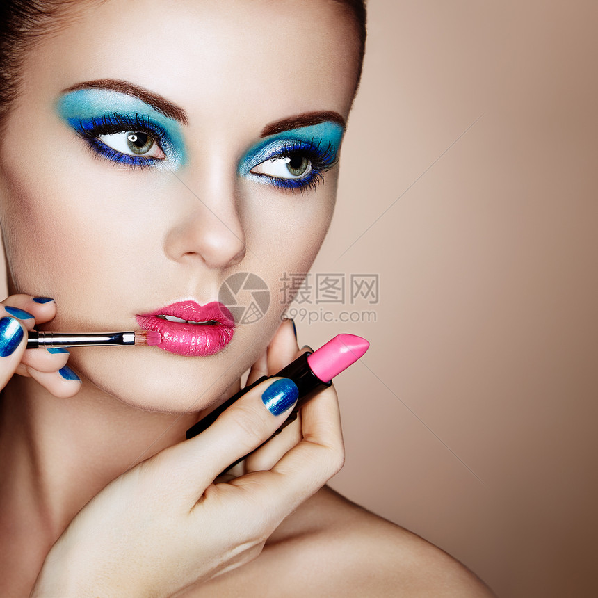 化妆师涂口红漂亮的女人脸化妆细节完美皮肤的美容模特粉红色的嘴唇蓝色的指甲修剪图片