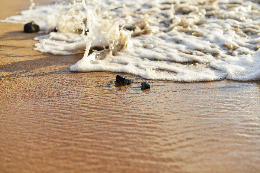 海边沙子上的石头被海浪冲走图片
