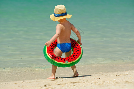 西瓜海洋两岁的蹒跚学步的男孩,海滩上充气游泳圈背景