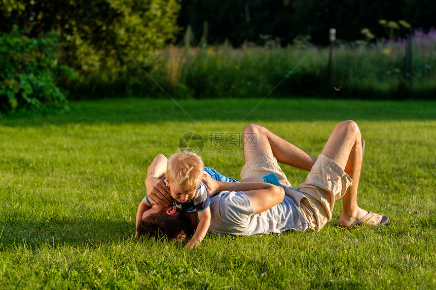 快乐的父子草地上玩得很开心快乐的人孩子草地上玩得很开心父亲儿子公园的绿草地上休息的家庭生活方式场景图片