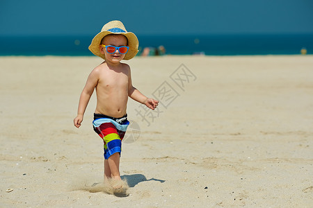 25秒两岁的蹒跚学步的男孩海滩上跑步两岁的蹒跚学步的男孩戴着太阳帽海滩上跑步背景