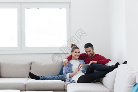 轻的夫妇家里放松,用平板电脑客厅沙发上看书图片