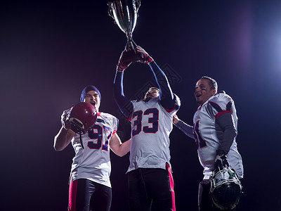 快乐的美国足球队带着奖杯庆祝夜间比赛的胜利图片