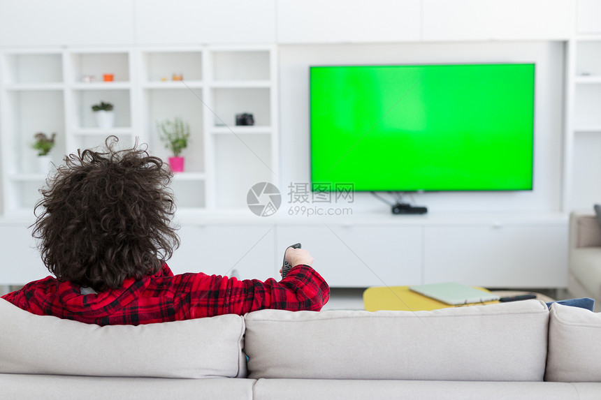 穿着浴袍的轻英俊的男人他豪华的家享受空闲时间看电视图片