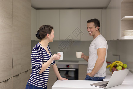 幸福的轻夫妇带着笔记本电脑现代厨房享受早晨的咖啡图片