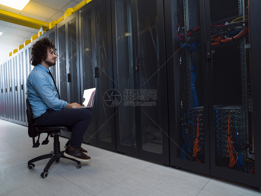 男IT工程师现代数据中心服务器机房的笔记本电脑上工作图片