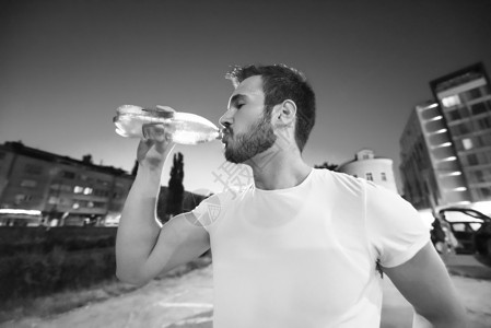 轻的运动男子城市的夜跑步后喝水图片